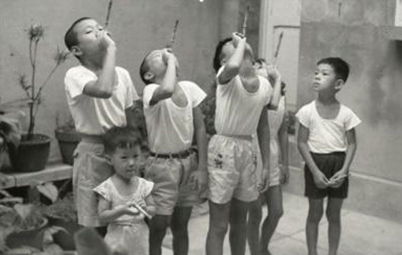 早期臺灣童玩老照片：六位孩童聚在一起玩「吹龍」口哨玩具。影像捕捉到孩子們吹氣時，捲曲紙管向前拉長伸直的動態神情，展現純真快樂的常民童年日常。