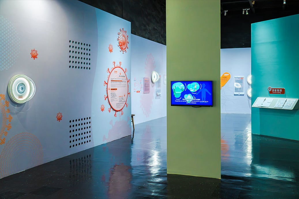 「看見你我他牠它」特展展區，淺綠柱體影片螢幕結合病毒圖文牆與「深度閱讀」閱覽台